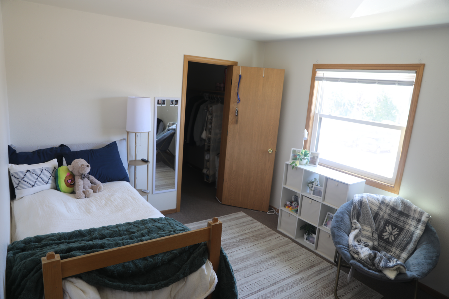 Bedroom with a closet, a bed with white and navy bedding, a white cube dresser, and a light blue chair.